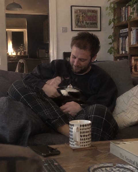 Ben on the sofa with his black and white cat asleep on his lap.