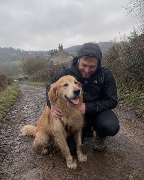 Tom crouching on a country lane with his golden retriever.